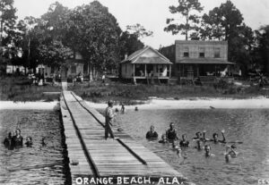 Black and white photo of people swimming by a wharf in Orange Beach