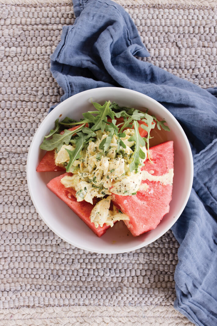 curried crab and watermelon salad plated in a white bowl on top of a textured place setting and next to a blue linen napkin