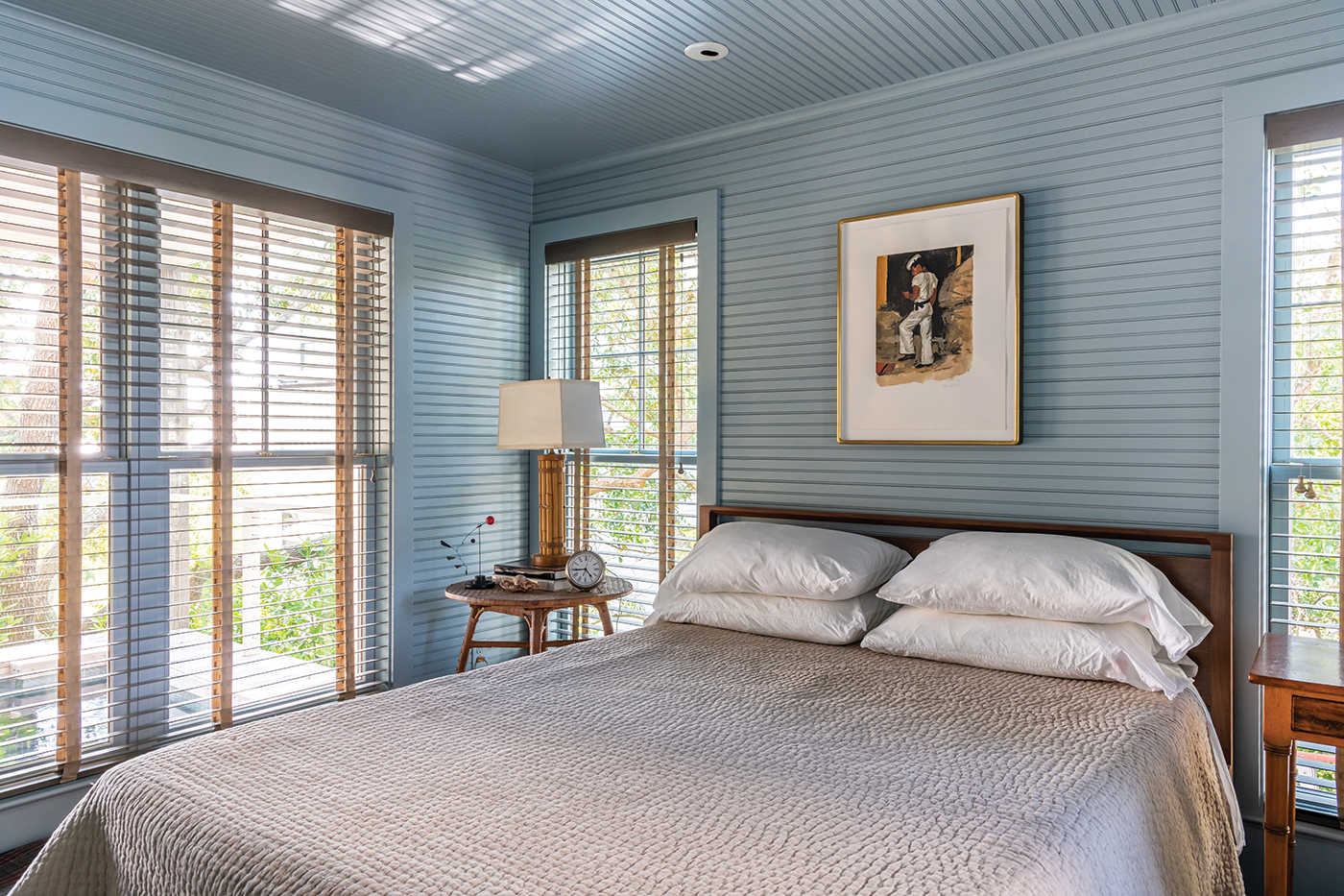 blue toned bedroom beaded board for the walls with mutiple windows and neautral bedsetting 