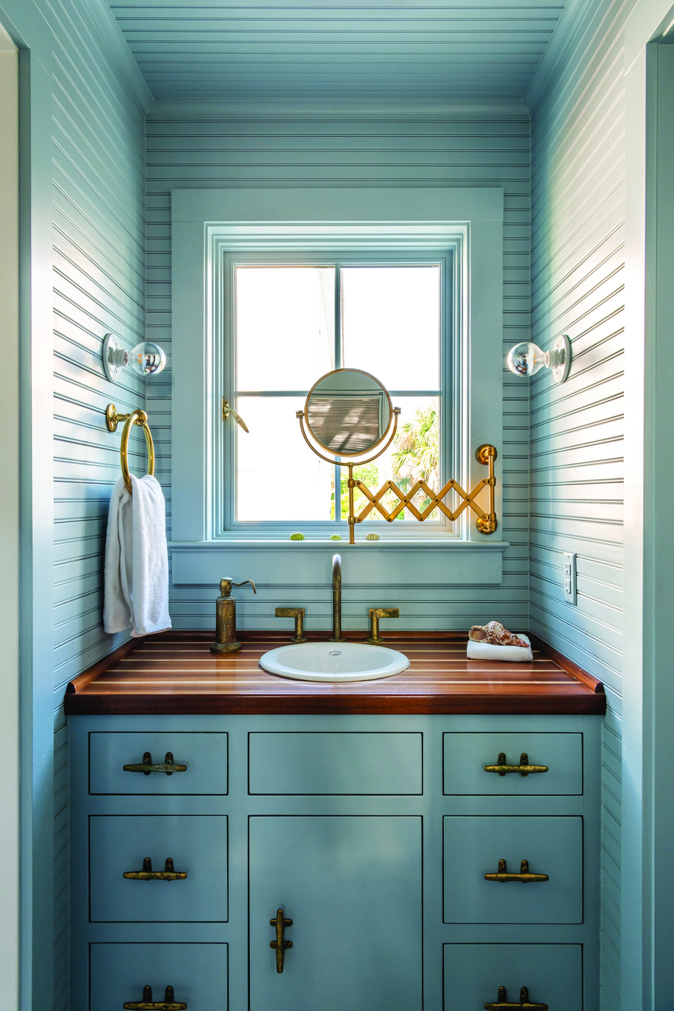 blue toned bathroom cabinets with nautical inspired details and a built in accordion style mirror stretched out in front of centered window