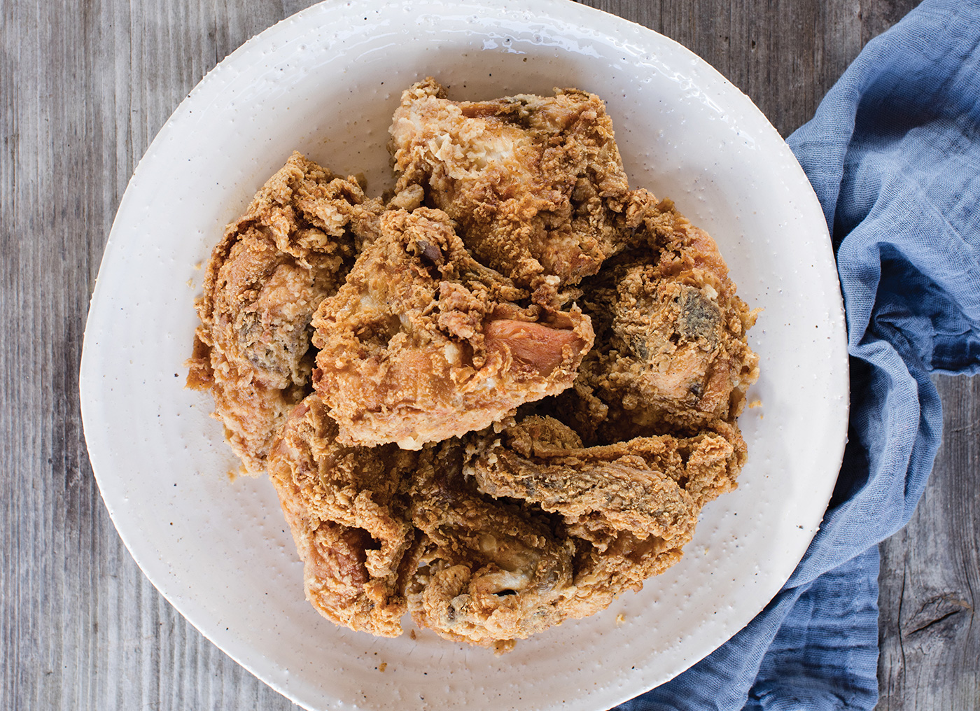 fried chicken plated upon a wood table next to a blue linen napkin 