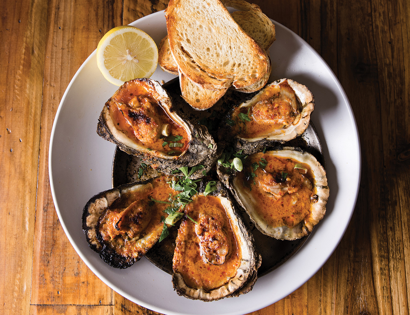 Roasted oysters served on a white plate with lemon and french bread on the side 