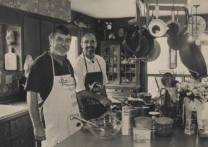 A black and white photograph of Dr. Bob Shipp and John Dindo cooking in a kitchen.
