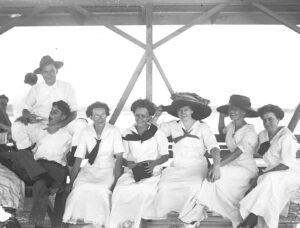 A vintage photograph of Mobile Bay-area residents dressed in the summer staple white cotton sitting on the wharf by the water.