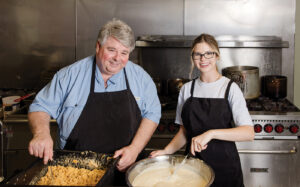 A male and female cook mixing up southern food in a restaurant kitchen.